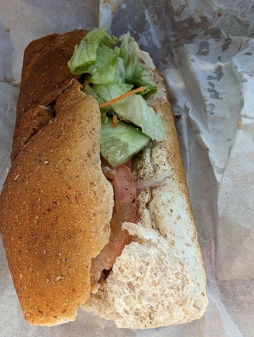 A granary roll filled with ham and lettuce, opened on its white paper wrapping